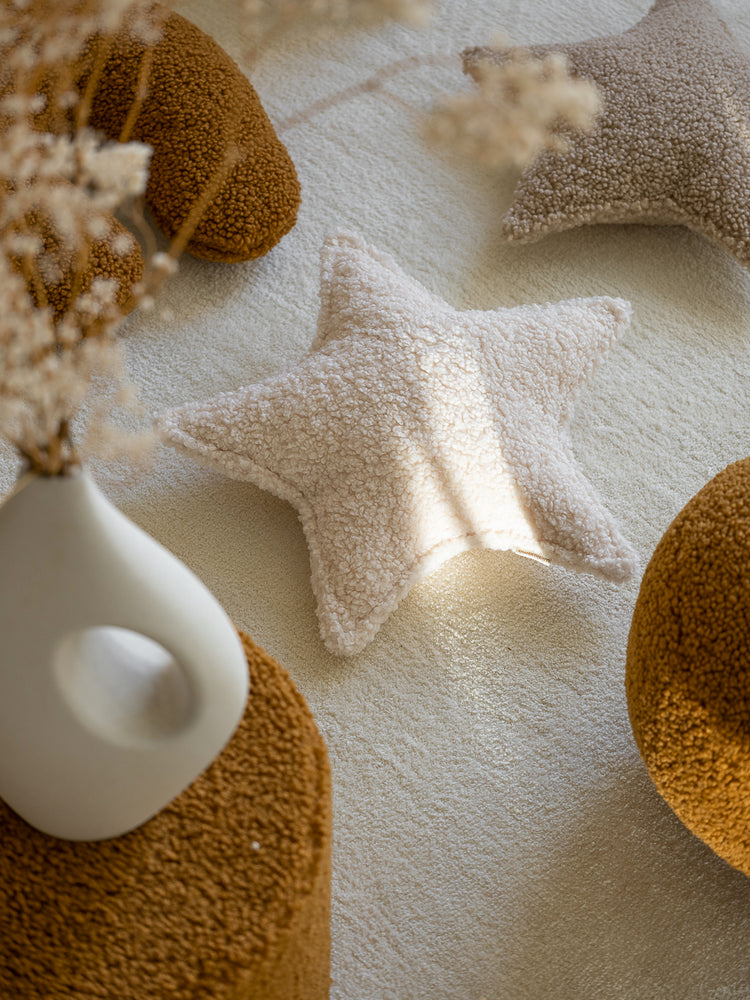 Coussin étoile en peluche coton Oeko-tex blanc crème illuminé par la lumière du soleil. WIGIWAMA