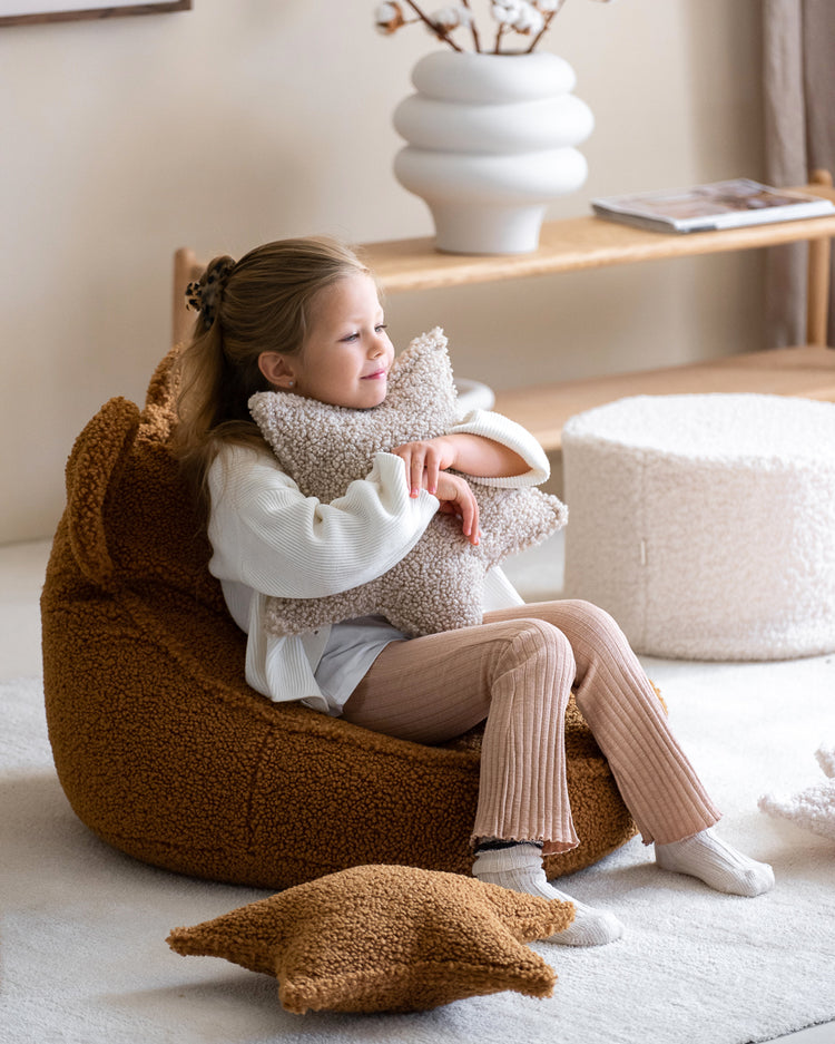 Petite fille câlinant un coussin étoile en peluche sur un fauteuil en moumoute en forme d'ourson. Idée déco pour aménager un coin lecture confortable dans un salon ou une chambre d'enfant.