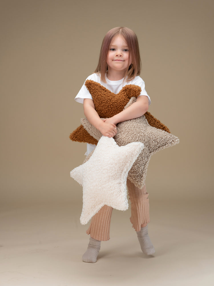Petite fille debout tenant dans ses bras des coussins en forme d'étoile pour chambre d'enfant. Wigiwama. Décoration responsable pour chambre d'enfant.
