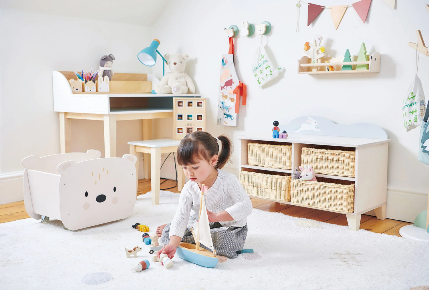 Décor de chambre d'enfants Tender Leaf, spécialiste du jouet en bois issu de forêt gérée durablement. Une petite fille s'amuse avec son bateau en bois dans sa chambre. 
