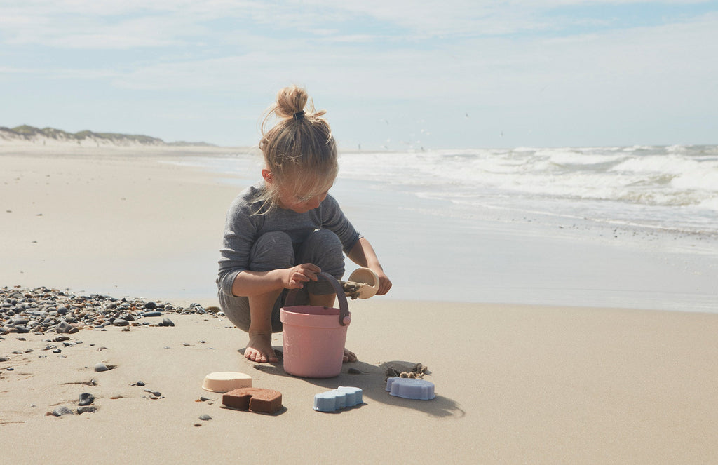 Jouets de plage en silicone pour enfant. Kit d'accessoire comprenant un seau, une pelle et 4 moules couleurs corail, beige, marron. Idéal pour une journée à la plage ou activités de plein air.