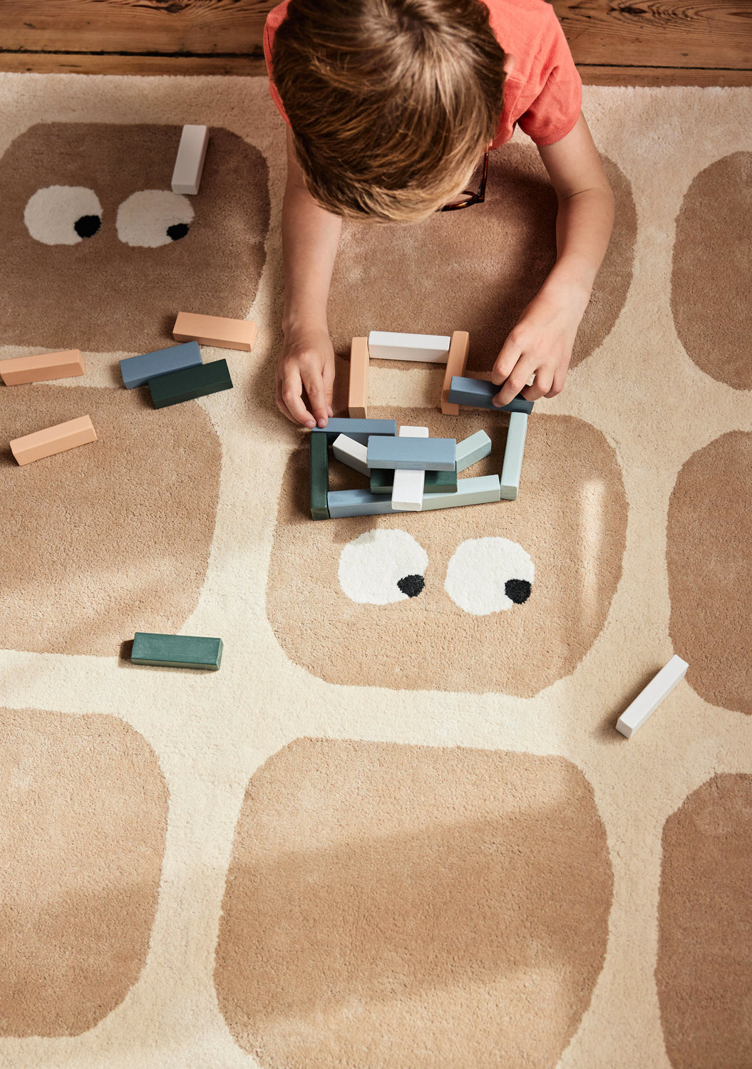 Enfant jouant sur un tapis rectangulaire en coton bio, motifs ludiques et petits yeux. Bidules, beige. Bleuu-studio.