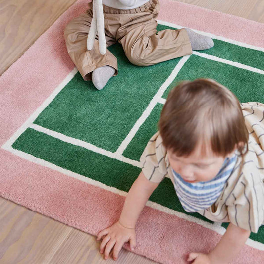 Enfants jouant sur un tapis rose et vert en forme de terrain de tennis, décoration chambre enfant thème sportif.